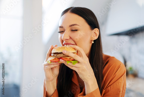 Wallpaper Mural Satisfied hungry lady biting tasty burger with pleasure, enjoying cheat meal for lunch in kitchen interior, closeup Torontodigital.ca