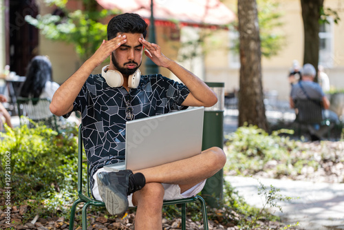 Hispanic young man using laptop computer typing browsing, loses becoming surprised sudden lottery results, bad news, fortune loss, fail. Guy sits in urban city street park outdoors. Town lifestyles. photo