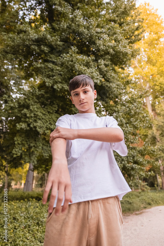 A young man in a white shirt and tan pants poses in front of a tree