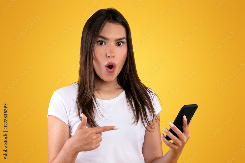 Wow, Breaking News. Portrait of surprised amazed young woman using smartphone and pointing at gadget with open mouth standing isolated on orange studio background. Lady chatting online Wow, Breaking News. Portrait of surprised amazed young woman using smartphone and pointing at gadget with open mouth standing isolated on orange studio background. Lady chatting online