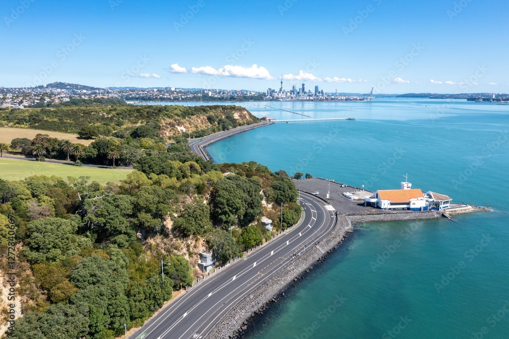 Fototapeta premium Aerial view of Tamaki Drive winding around a harbor, empty with a marina and city skyline in the background. Empty during Covid 19 lockdowns. Orakei, Auckland, New Zealand