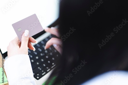 A close-up shot of a woman holding a credit card while looking at a laptop screen, possibly reviewing financial details or making an online transaction. photo