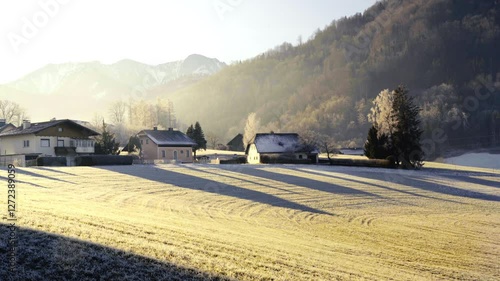 A serene winter morning in a rural village with frost-covered fields, traditional houses, and mountains in the background under soft sunlight. 4K