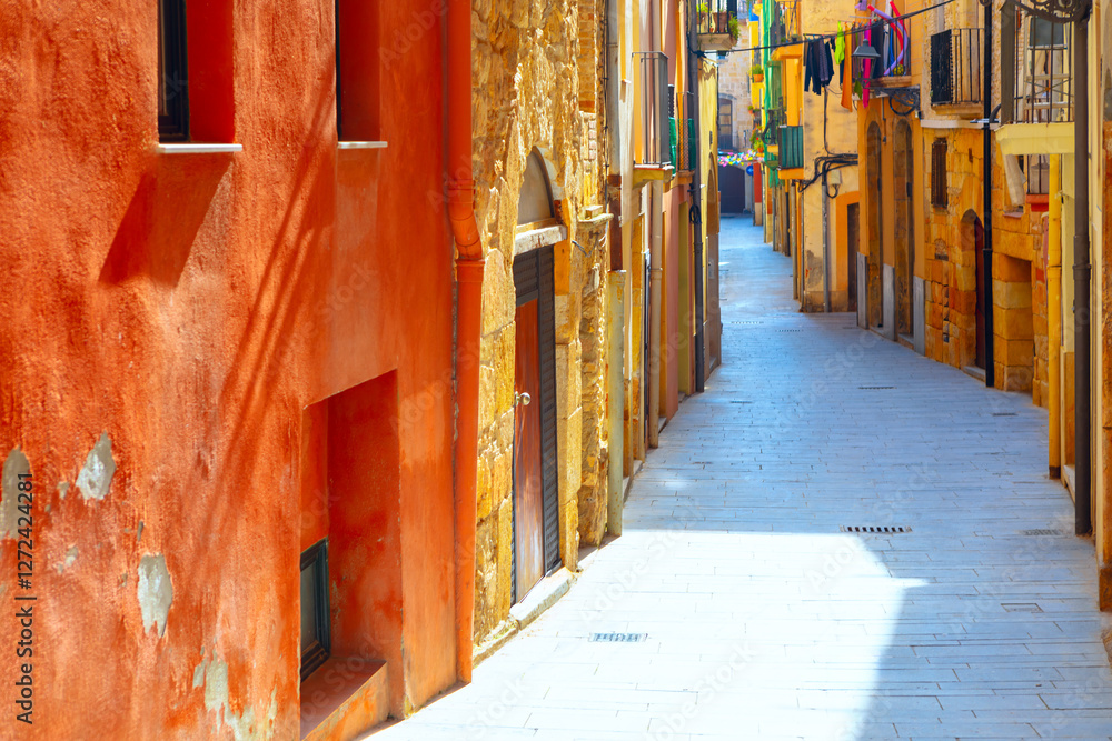 Sunlit old street in Tarragona with colorful, weathered facades and charming medieval architecture. Peaceful narrow alley with vibrant laundry hanging above, capturing essence of historic Catalonia