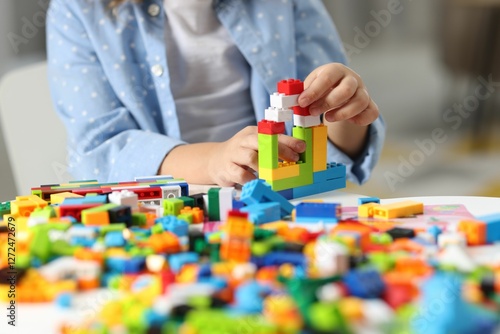 Girl playing with building blocks at white table indoors, closeup