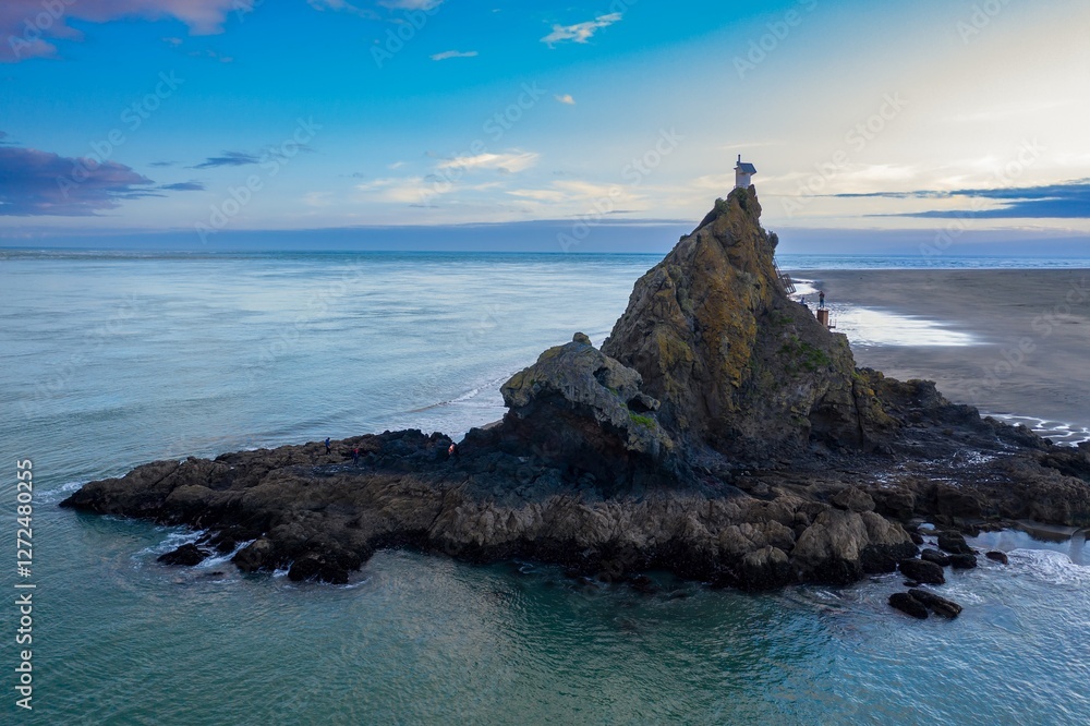 Coastal rock formation at Whatipu with small lighthouse atop, people exploring the rocky shore. Dramatic coastal scenery., Auckland, New Zealand Coastal rock formation at Whatipu with small lighthouse atop, people exploring the rocky shore. Dramatic coastal scenery., Auckland, New Zealand