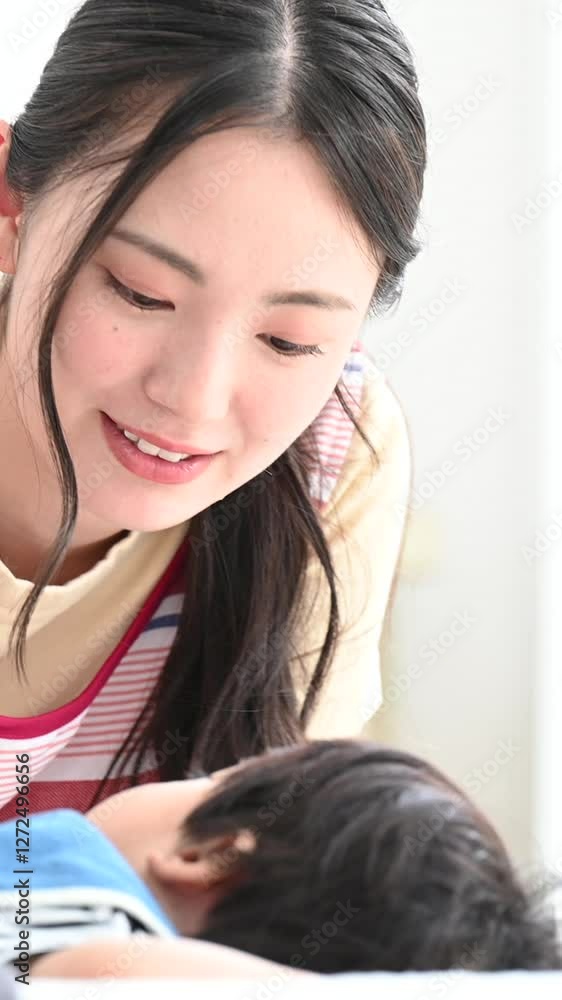 Close-up of a vertical video of a mother and nursery worker putting her baby to sleep in a brightly lit living room