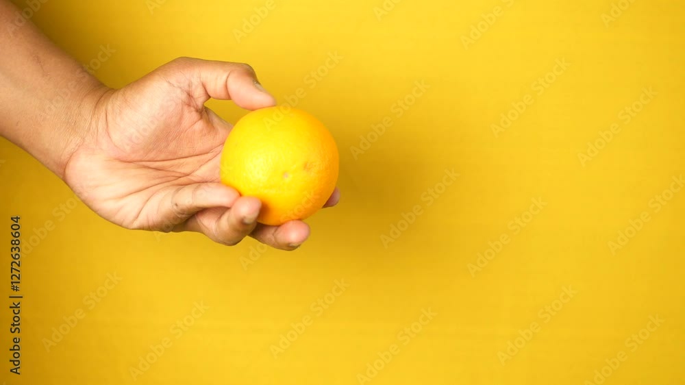 Person holding a bright orange in front of a yellow background Person holding a bright orange in front of a yellow background
