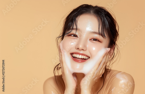 Smiling young woman with glowing skin, applying cleanser on her face against peach background. photo