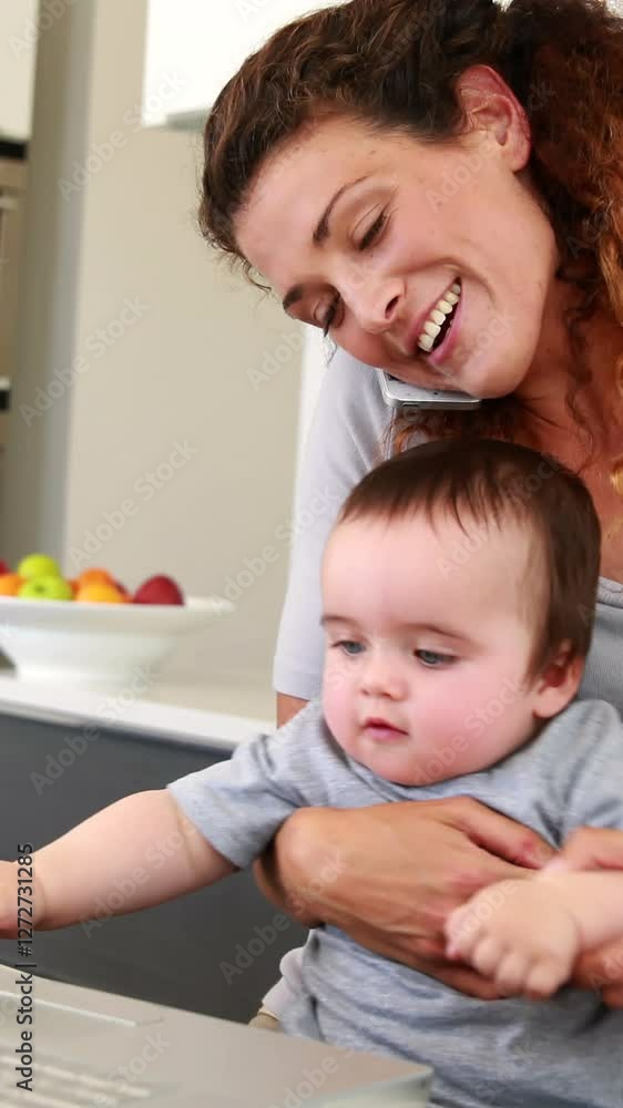 Mother sitting with baby boy on lap using laptop and talking on phone Mother sitting with baby boy on lap using laptop and talking on phone