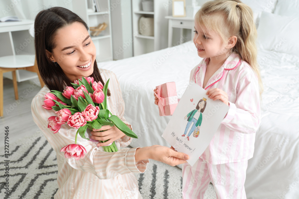 Little girl congratulating her happy mom with bouquet of beautiful flowers and greeting card in bedroom. Mother's Day celebration Little girl congratulating her happy mom with bouquet of beautiful flowers and greeting card in bedroom. Mother's Day celebration