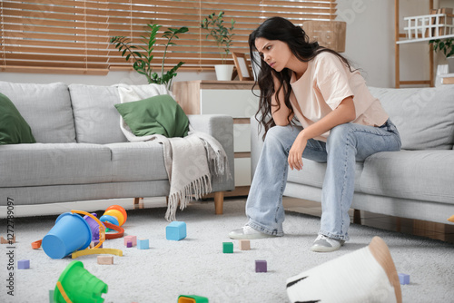 Tired young mother resting among scattered children's toys at home. Stress co...