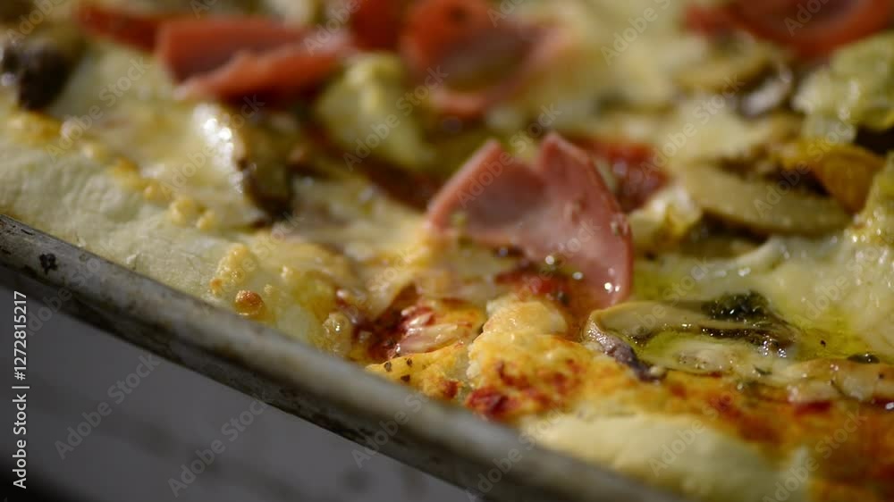 A close-up video of a homemade rectangular pizza topped with ham, artichokes, cheese, and red peppers, ready for baking. A close-up video of a homemade rectangular pizza topped with ham, artichokes, cheese, and red peppers, ready for baking.