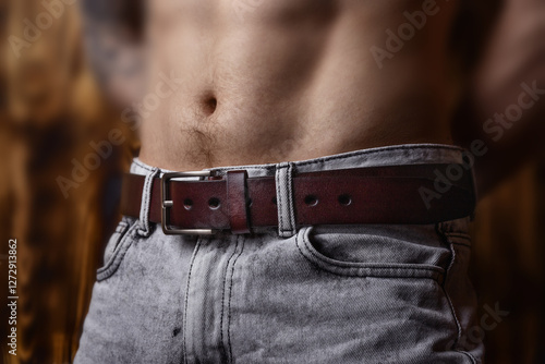 pumped-up young man with bare torso and light jeans with belt poses in front of the camera, close-up photo