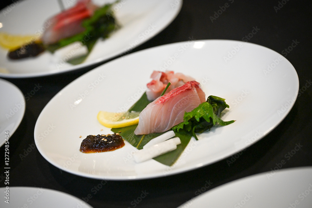 Sliced fish is artfully placed on a bed of greens, garnished with fresh lemon and a rich sauce, showcasing the elegance of Japanese culinary presentation. Sliced fish is artfully placed on a bed of greens, garnished with fresh lemon and a rich sauce, showcasing the elegance of Japanese culinary presentation.