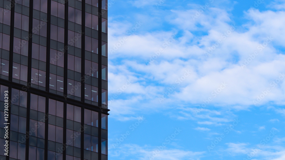 A modern glass building on the left with reflective panels, contrasting against a bright blue sky with scattered white clouds.