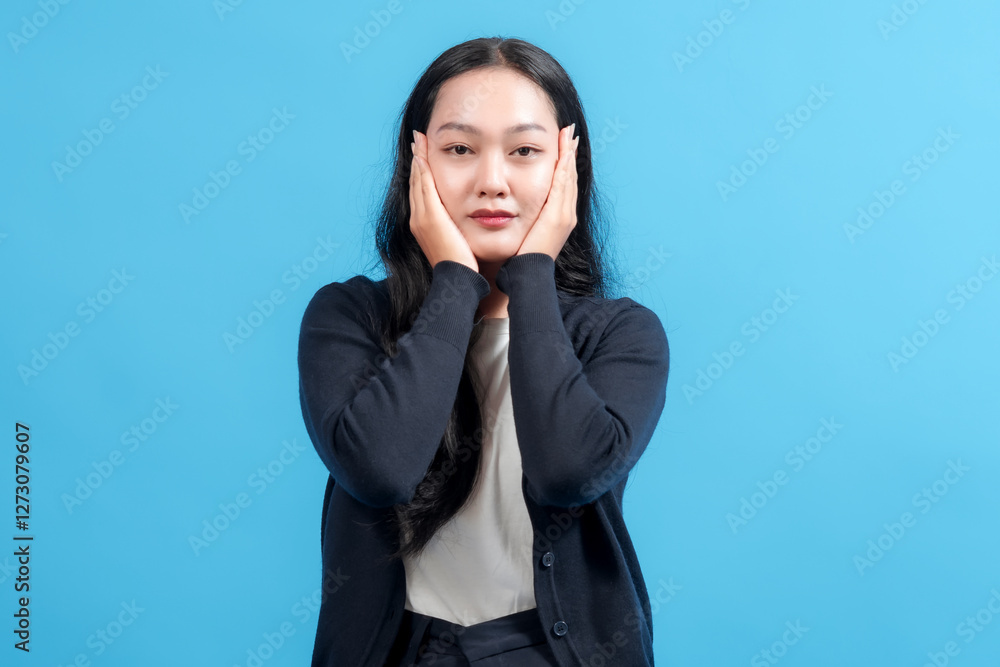 Portrait of a woman with a thoughtful expression, standing against a vibrant blue background and resting her hands on her face, evoking calmness and contemplation. Portrait of a woman with a thoughtful expression, standing against a vibrant blue background and resting her hands on her face, evoking calmness and contemplation.