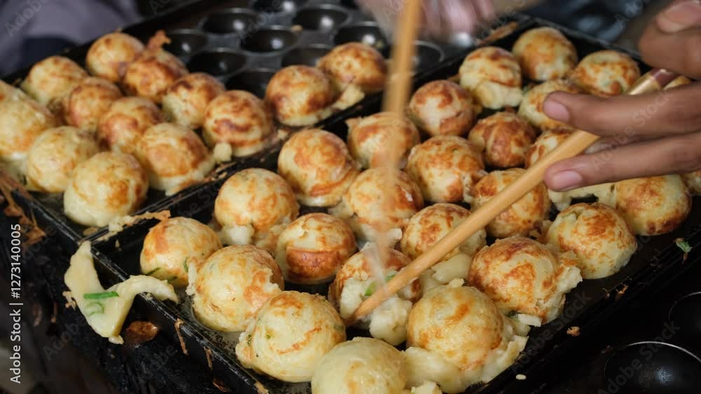 close up, Japanese street food vendor's hand flipping cooked takokayi balls using chopsticks on an iron mold close up, Japanese street food vendor's hand flipping cooked takokayi balls using chopsticks on an iron mold