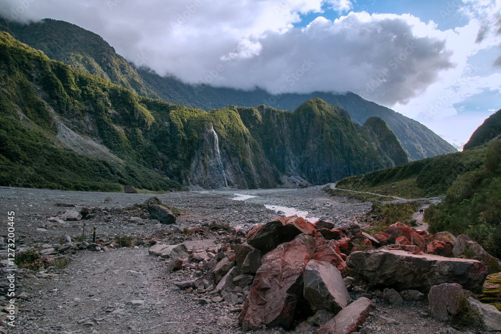 Fototapeta premium Franz Josef Glacier Walk rocky terrain along the glacial valley with rugged mountains in the background under a cloudy sky
