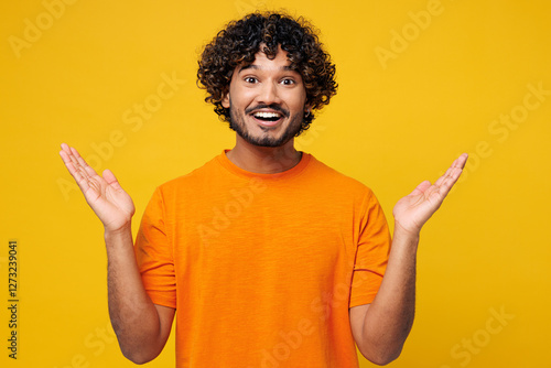 Young smiling shocked surprised impressed amazed happy Indian man he wear orange t-shirt casual clothes look camera spread hands isolated on plain yellow background studio portrait. Lifestyle concept. photo