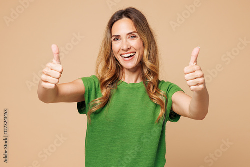 Young smiling happy cheerful fun cool woman she wearing green t-shirt casual clothes showing thumb up like gesture isolated on plain pastel light beige background studio portrait. Lifestyle concept.