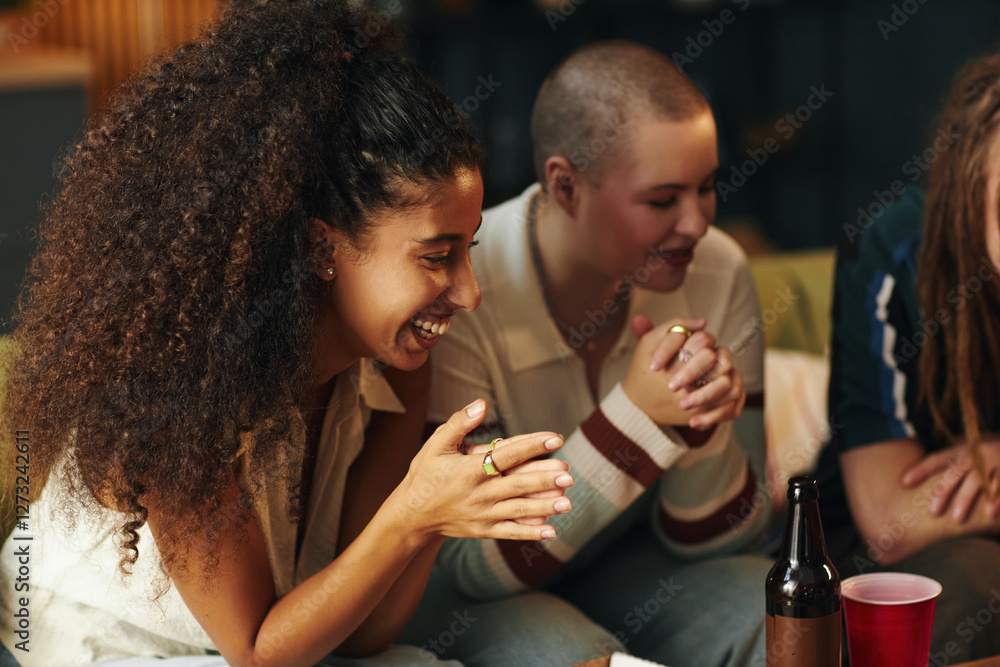Multiracial group of friends enjoying conversation in a cozy indoor environment, sharing laughter while sitting close together and engaging in friendly interaction Multiracial group of friends enjoying conversation in a cozy indoor environment, sharing laughter while sitting close together and engaging in friendly interaction