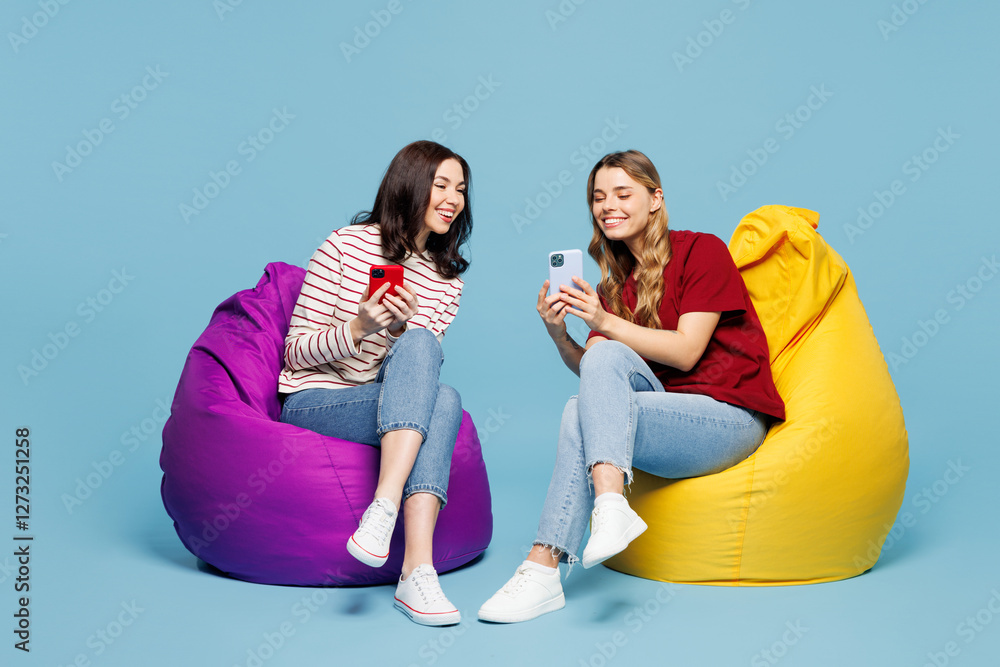 Φωτογραφία Full body young couple two friends women wearing red casual clothes together sit in bag chair hold in hand use show mobile cell phone isolated on pastel plain light blue background