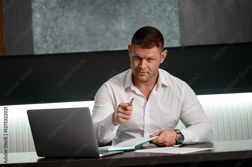 Businessman using laptop while sitting on chair in office. Young businessman sitting at his desk in the office. Businessman sitting at the table looking into the lens and pointing with a pen. Businessman using laptop while sitting on chair in office. Young businessman sitting at his desk in the office. Businessman sitting at the table looking into the lens and pointing with a pen.