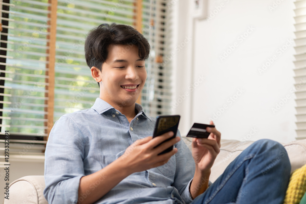 man sitting on couch holding smartphone and credit card, smiling while making online purchase in bright living room with natural light man sitting on couch holding smartphone and credit card, smiling while making online purchase in bright living room with natural light