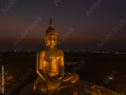 aerial view The moon was above the head of the biggest golden Buddha in the world..scenery red sky in twilight background. .golden big buddha is a popular landmark at wat Muang Ang Thong Thailand. photo