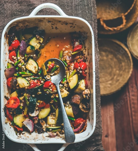 Verduras al horno con calabacín, cebolla, tomates, champiñones, aceite de oliva y especias en una fuente para el horno de color blanco. Un plato bajo en calorías. photo