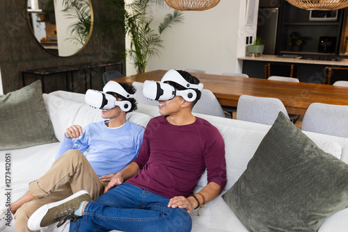 A gay couple with VR headsets enjoy virtual experience on couch photo