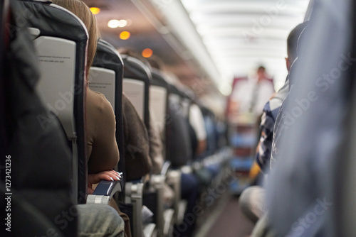 A male steward who distributes food and drinks on board the aircraft. The passengers are sitting in their seats and watching. View along the row. High quality photo