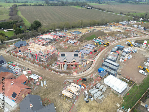Drone view of new homes being developed in rural Essex, UK. In the distance is arable farmland. Roof beams can be seen on the detached house in the middle of the image.