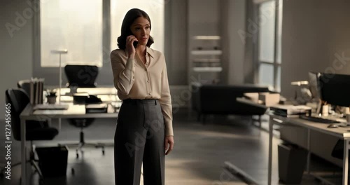 A businesswoman is talking on the phone while standing in an office