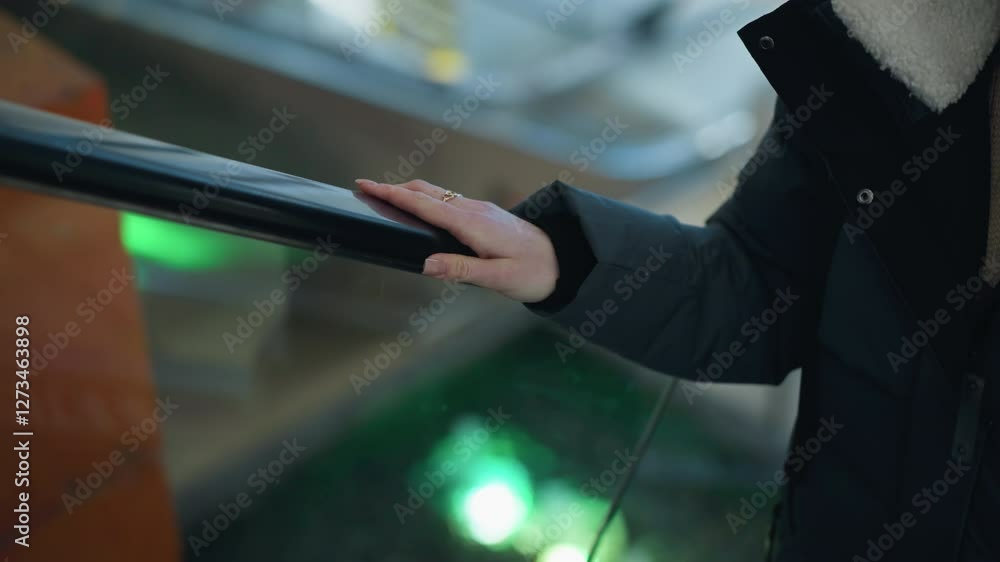Close-up of hand with a ring placed on rail of moving escalator with colorful blinking lights reflecting in blurred background, escalator ascending in shopping mall environment Close-up of hand with a ring placed on rail of moving escalator with colorful blinking lights reflecting in blurred background, escalator ascending in shopping mall environment