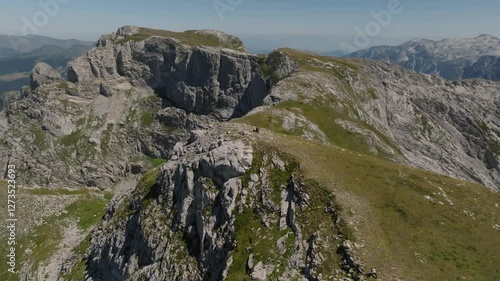 Cinematic drone shot flying away from the summit of Zla Kolata mountain with tourists on it, with the mountains of Albania and Montenegro in the background in summer