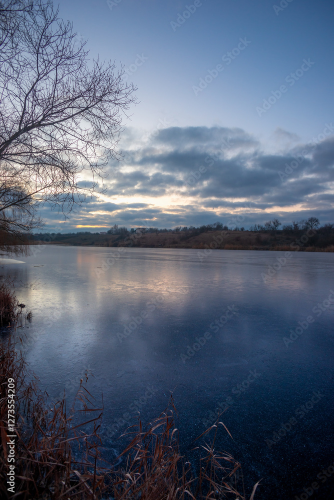 Obraz premium Beautiful blue hour on the lake, trees on the beach , sunrise over the lake with blue sky without clouds.Landscape photography on the pond , purple colors on the sky , trees and water , reflections 