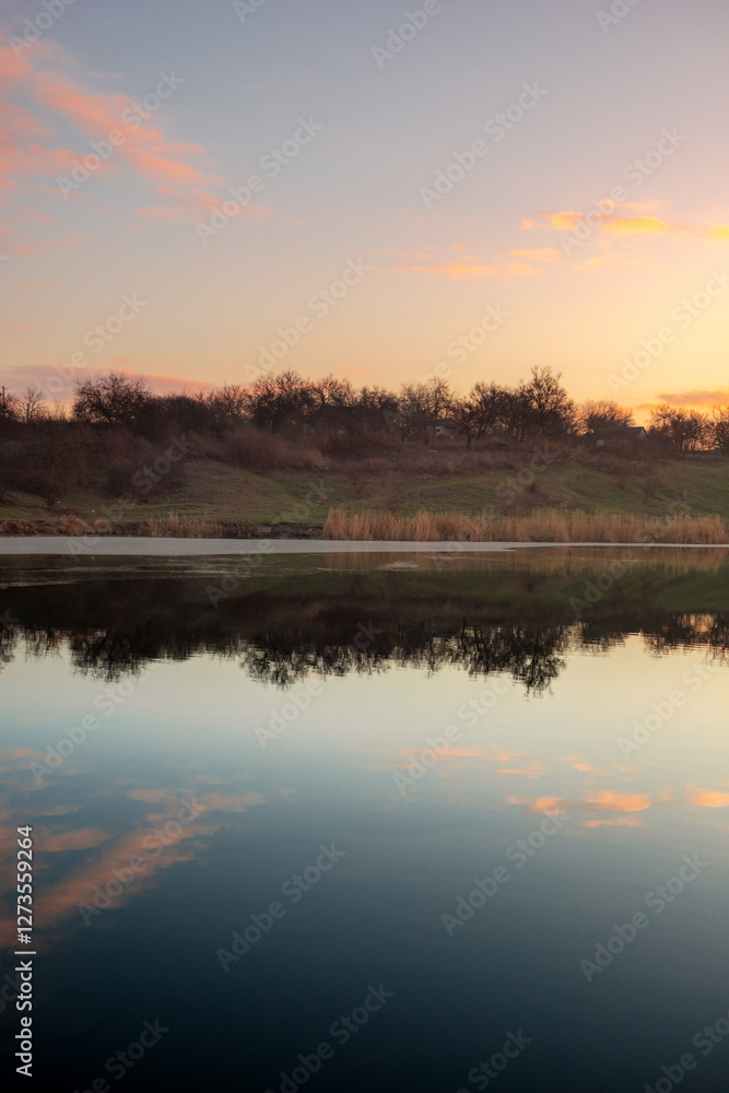 Fototapeta premium Blue hour on the lake , beautiful landscape photography on the lake with sunrise and reflactions on water , trees on the beach of the lake ,blue and orange colors.Blue sky . Water reflections 