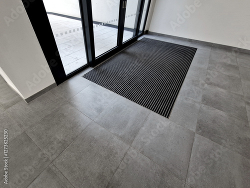 industrial mat cleaning zones at the entrance to the building. A black plastic-metal mat in the shape of an arch or half-circle lies on the limestone mosaic tiles
