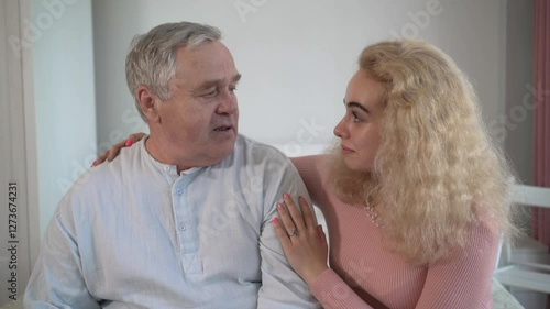 Senior man and young woman sitting together, talking with warm emotions. Family relationships, intergenerational bonding, elderly care, empathy, psychological support at home.