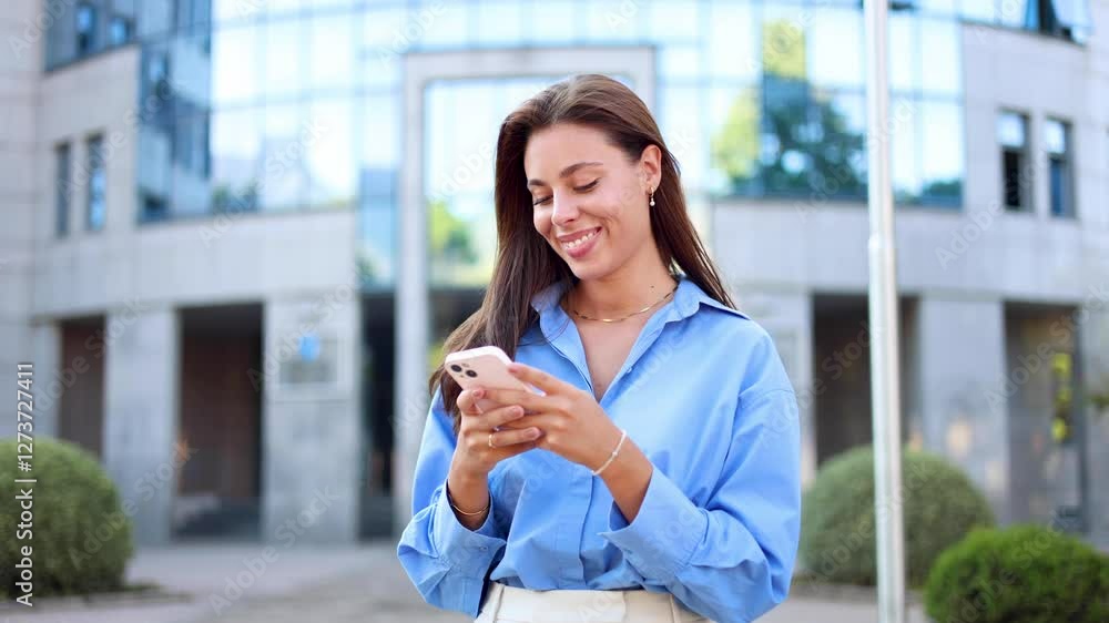 Gorgeous woman is smiling while using her smartphone on the sidewalk