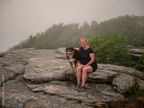 Portrait of smiling woman with Black Tri Australian Shepard sitting on rocks photo