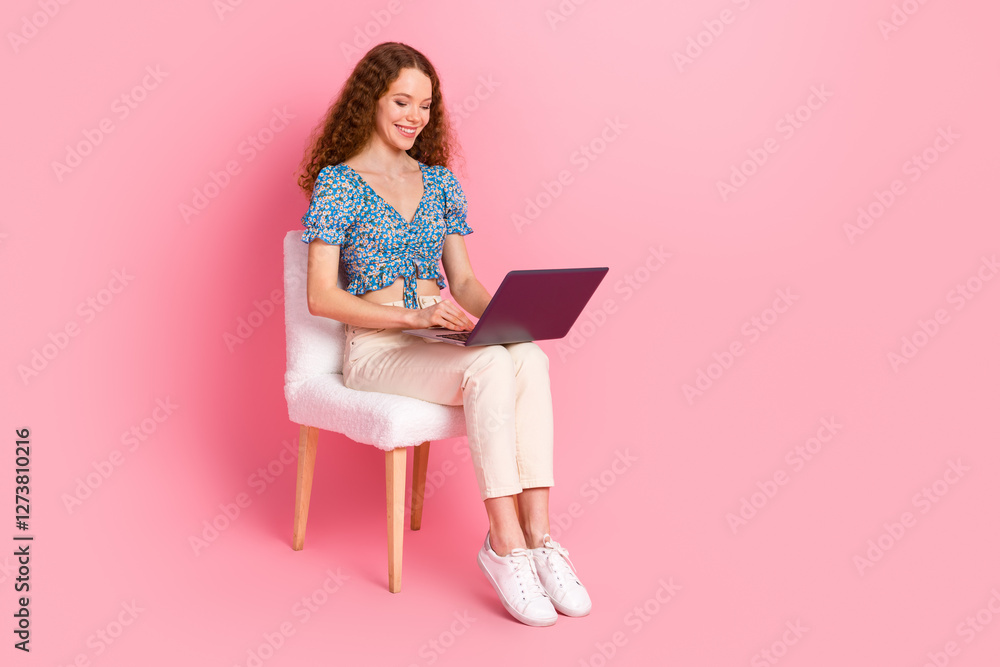 Smiling woman using laptop against pink background in casual attire Smiling woman using laptop against pink background in casual attire