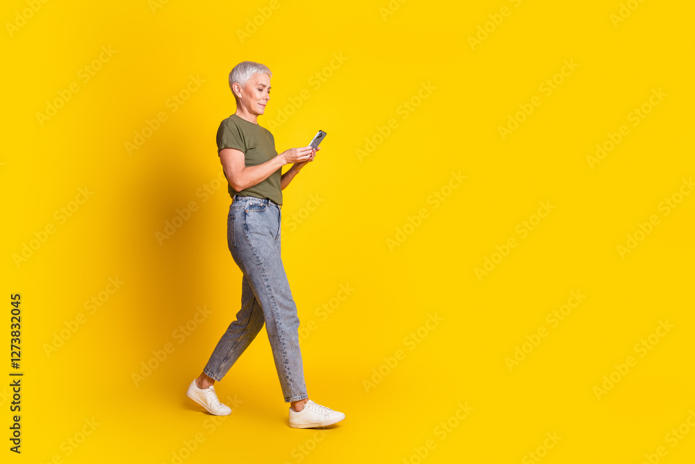 Full length photo of shiny attractive lady dressed khaki t-shirt walking typing modern gadget empty space isolated yellow color background Full length photo of shiny attractive lady dressed khaki t-shirt walking typing modern gadget empty space isolated yellow color background