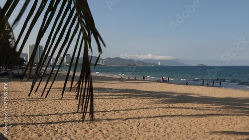 Public beach in Nha Trang, Vietnam. Beautiful view of the embankment, mountains, beach and South China Sea. Tourists and locals relax and swim. Handheld shooting in slow motion. Overview.