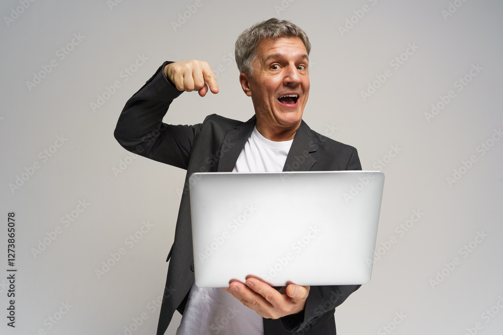Older man in a suit enthusiastically showcases a laptop during a studio session Older man in a suit enthusiastically showcases a laptop during a studio session