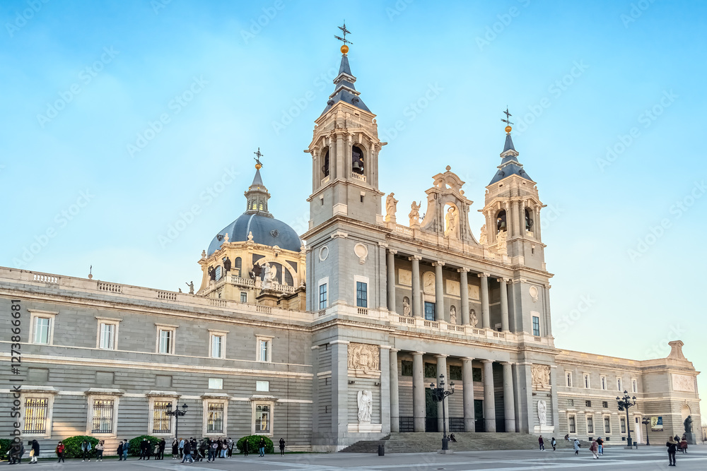 Naklejka premium Almudena Cathedral in Madrid, showcasing its neoclassical architectural style with twin bell towers and an impressive dome. Visitors are seen exploring the area. Madrid, Spain - November 30, 2021