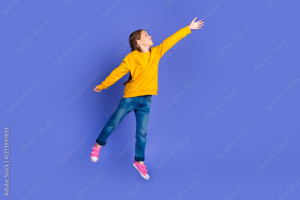 Young girl in yellow sweatshirt and jeans leaping against a vivid purple background showcasing playful energy and happiness Young girl in yellow sweatshirt and jeans leaping against a vivid purple background showcasing playful energy and happiness