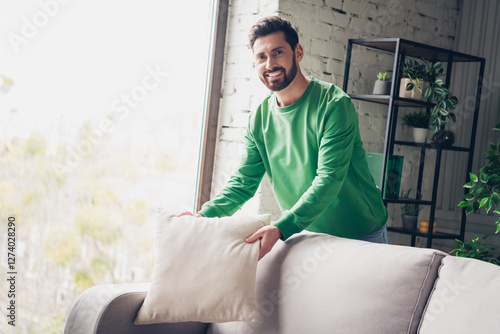 Bilde på lerret Young man in casual green top arranging a cushion in a modern living room with natural daylight and cozy decor